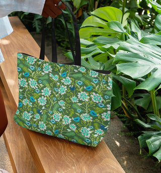 Green floral-patterned tote bag on a wooden bench with plants in the background