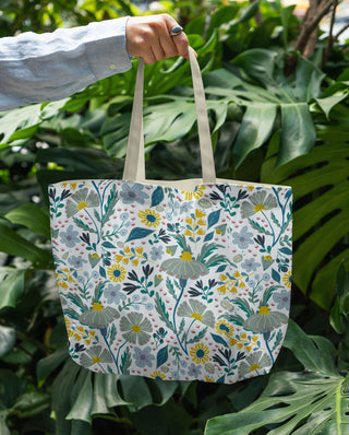 Tote bag with hand drawn floral pattern held by a hand against a green leafy background. sold online at jean c studio