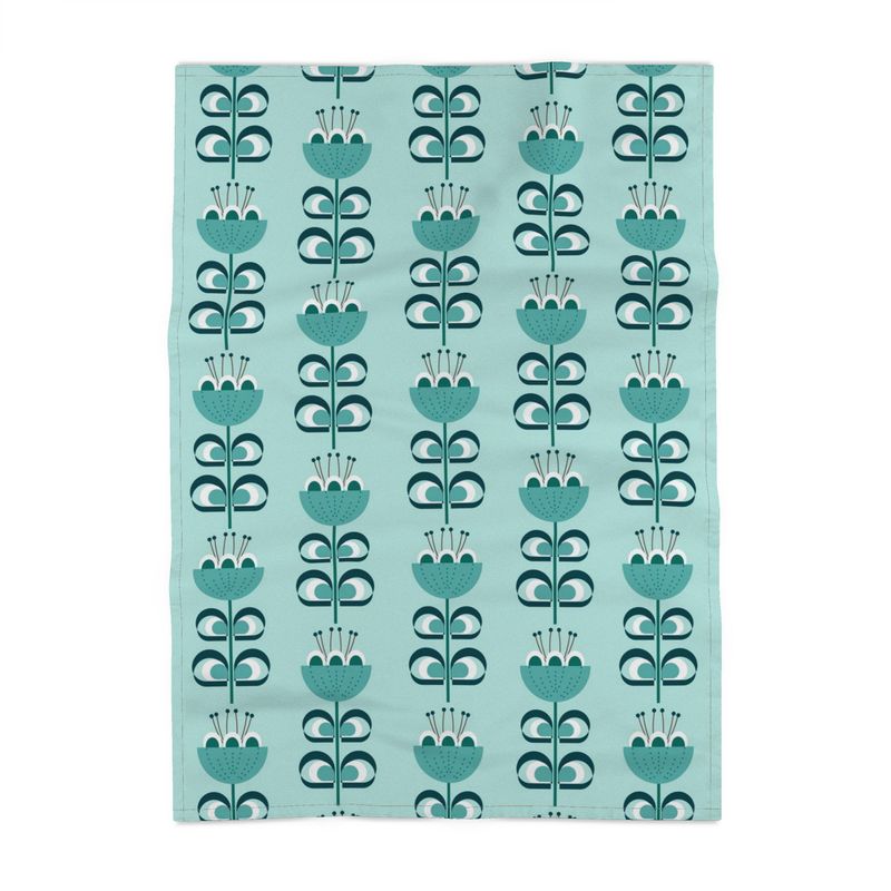 image of a cotton tea towel with stylized flowers in a color palette of blue green and dark green. The flowers resemble tulips. The background is a pale blue green.
