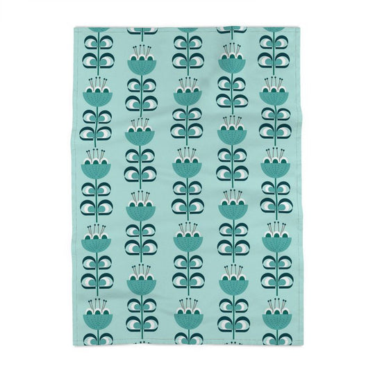image of a cotton tea towel with stylized flowers in a color palette of blue green and dark green. The flowers resemble tulips. The background is a pale blue green.