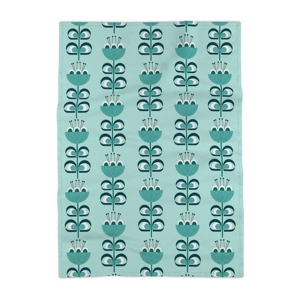 image of a cotton tea towel with stylized flowers in a color palette of blue green and dark green. The flowers resemble tulips. The background is a pale blue green.