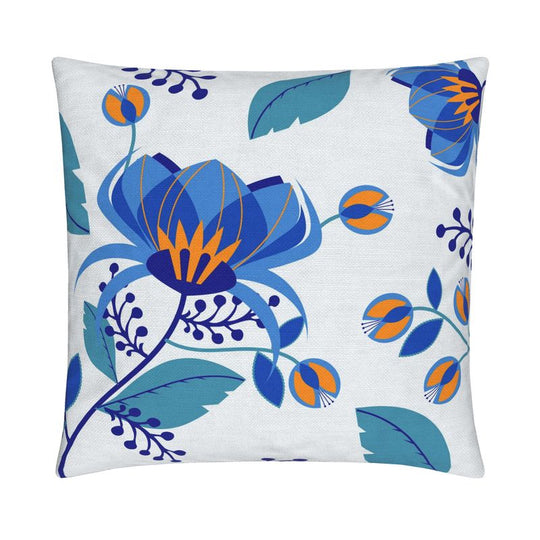 closeup image of a throw pillow. the pillow has a lot of abstract flowers in a palette of blues  with pops of orange. There are abstract blue leaves surrounding it. There are also cobalt blue berries in the background. The background is fresh white color.