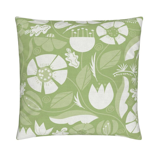 closeup image of a throw pillow. the pillow has a lot of abstract flowers in a palette of cream  and pale green. There are abstract green and white leaves surrounding it. There are also yellow green leaves in the background. The background is a fresh medium green color. It's a very summery or spring pillow cover.
