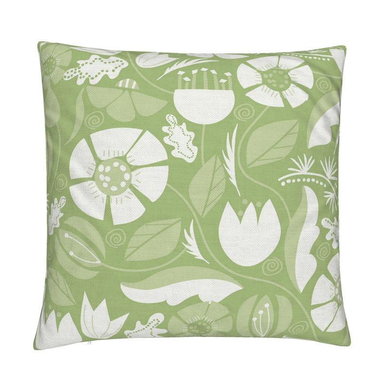 closeup image of a throw pillow. the pillow has a lot of abstract flowers in a palette of cream  and pale green. There are abstract green and white leaves surrounding it. There are also yellow green leaves in the background. The background is a fresh medium green color. It's a very summery or spring pillow cover.