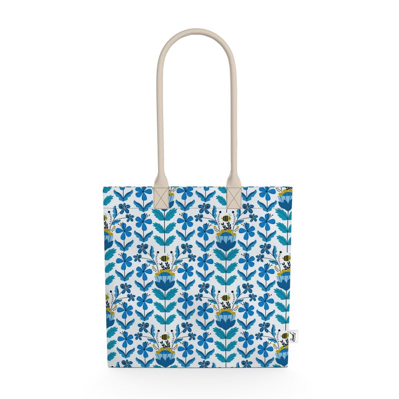 Image of tote bag with stylized blue and gold flowers, blue green leaves and bees