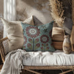 image of a throw pillow on a sofa. the pillow has a light teal background and 4 stylized brown and white flowers. Smaller dark green and light green flowers are in the background. 