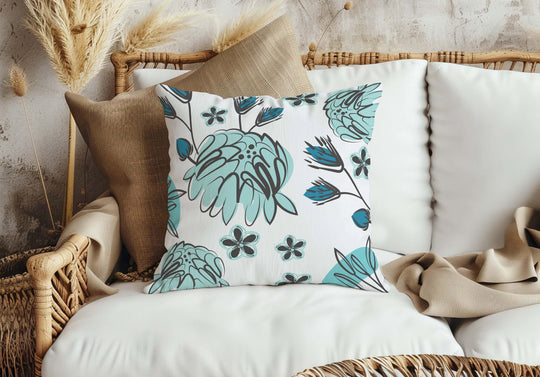 closeup image of a throw pillow on a sofa. the pillow has light blue stylized peonies and stylized blue and charcoal flowers. Smaller light blue and charcoal flowers are in the white background. The illustration is done in a brushy style.